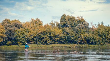 A fisherman casts a spinning rod while standing in a river.の写真素材