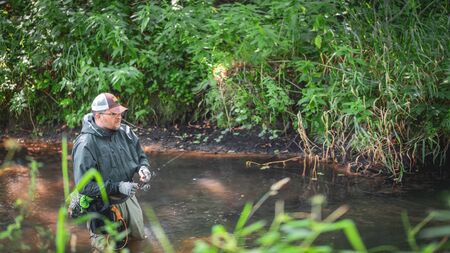 A fisherman catches spinning in the waders. Trout fishing.の写真素材