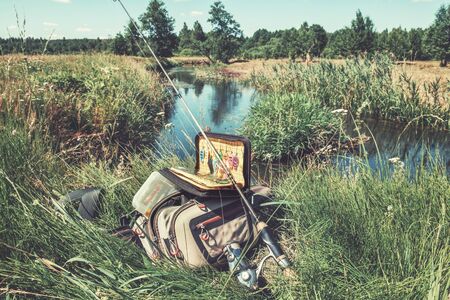 Bag with fishing essentials at riverside on sunny dayの写真素材