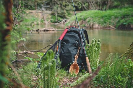 Backpack and fishing rod on the river. Fishing gear.