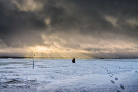 Fisherman on a background of storm clouds. Winter ice fishing on the lake.