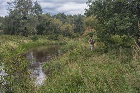 Fisherman on the shore of a small forest river.の写真素材