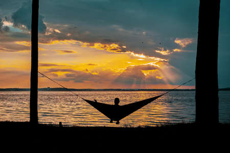 The girl is resting in a hammock on a sunset background.の写真素材
