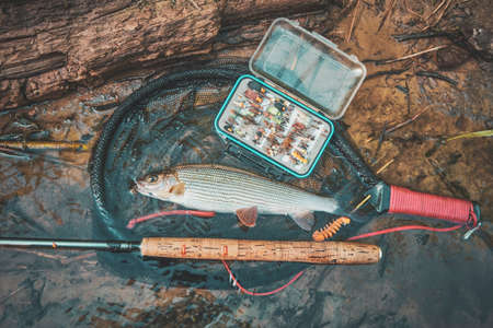 Landing net and box with flies against the background of grayling and stream.