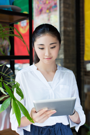 happy young woman drinking coffee / tea and using tablet computer in a coffee shopの写真素材