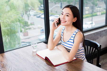 smiling young chinese woman talking on phone in a cafeの写真素材