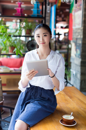girl sitting on a table in a cafe and holding a tabletの写真素材
