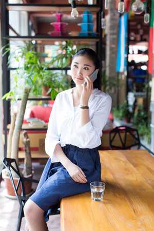 young black hair woman talking on the cellphone sitting on a table in a cafeの写真素材