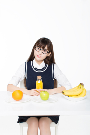 girl sitting in a classroom, apples and oranges arrayed on the desk as well as milk.の写真素材