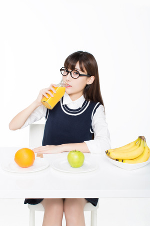 girl sitting in a classroom, apples and oranges arrayed on the desk as well as milk.の写真素材