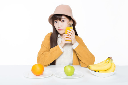 girl sitting in a classroom, apples and oranges arrayed on the desk as well as juice.の写真素材
