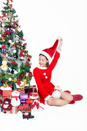 Pretty girl is sitting next to Christmas tree on white backgroundの写真素材
