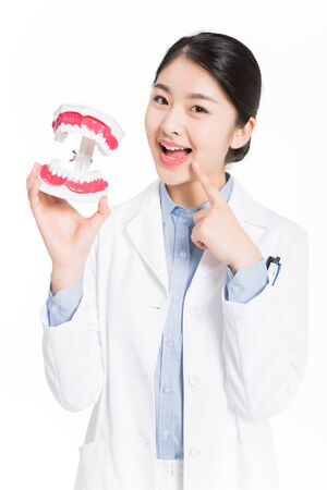 Young woman in surgical gown holding a dental teeth model and making cute gesture