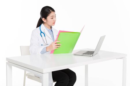 Female doctor in surgical gown checking documents in a fileの写真素材