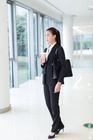 pretty girl wearing a black suit, standing in office buildingの写真素材