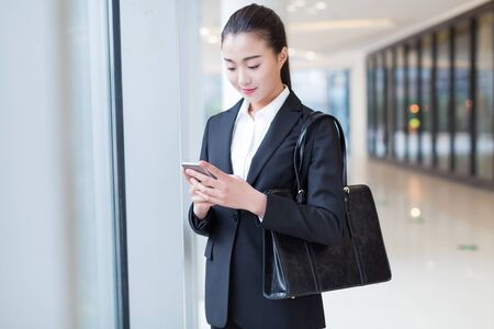 pretty girl wearing a black suit, standing in office buildingの写真素材