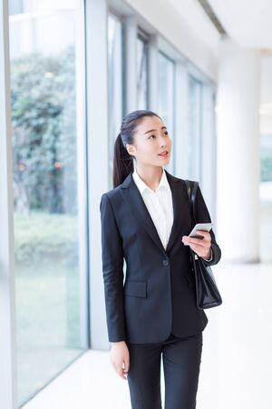 pretty girl wearing a black suit, standing in office buildingの写真素材