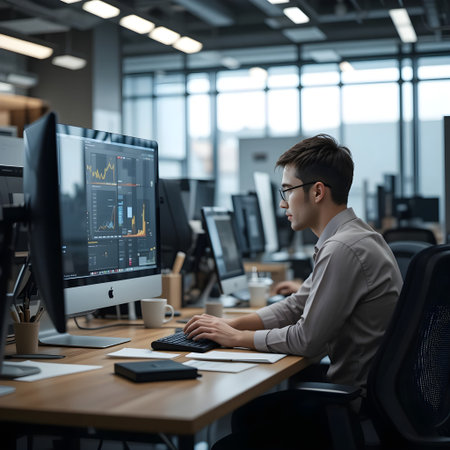 young businessman in eyeglasses using computer while sitting at desk in officeの素材