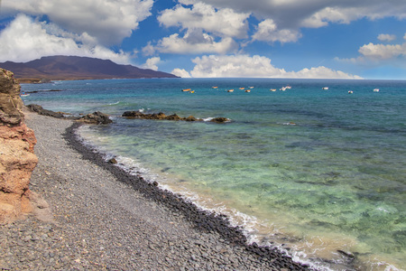 Stone beach of Puerto de la Cruze at Canary Islands, Fuerteventura, Spain. There are turquoise water of ocean and beautiful landscape with blue sunny sky and clouds.の写真素材