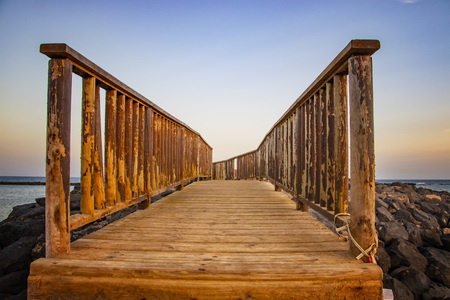 The wooden bridge overlooking the sea leads to an island at sunset. It is located in Fuerteventura, Canary islands.の写真素材