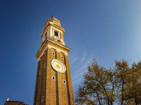 The beautiful old tower in Venice in Italy. There are summer time and blue sky with white clouds.