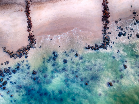 Aerial view of sandy beach with waves, clear ocean water and big black stones. It is tropical...