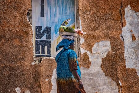 Saloum, Senegal, APRIL 26, 2019: Unidentifed Senegal woman carrying a watermelon and other fruits on...