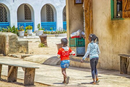 Goree island, Senegal- April 22 2019: Unidentified girls walk along a sandy street in a small town. It's a beautiful sun day.のeditorial素材