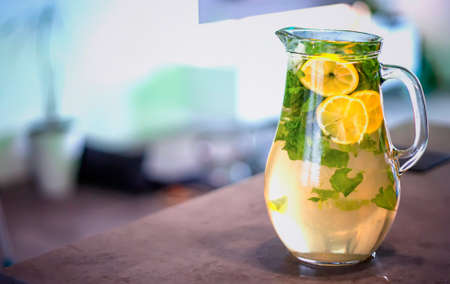 Ice cold lemonade with mint and lemon. The pitcher is standing on the kitchen counter. Background is blurred.の写真素材