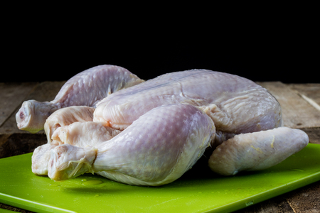 Raw chicken on a wooden board in an old kitchen, black backgroundの写真素材