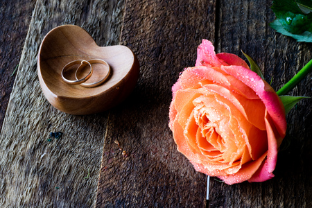Wet rose, heart and wedding rings on a wooden tableの写真素材