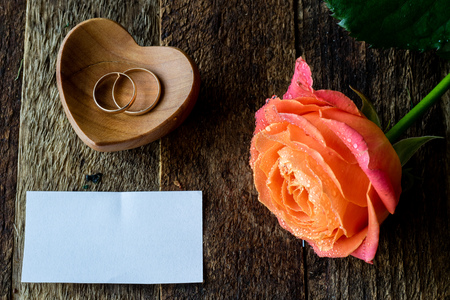 Wet rose, heart and wedding rings on a wooden tableの写真素材