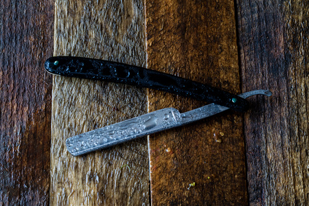 Wet razor on a wooden table, black background.の写真素材
