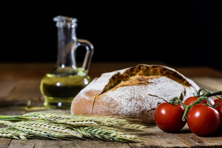 Tasty country bread and red cocktail tomatoes. Black background and wooden table.の写真素材