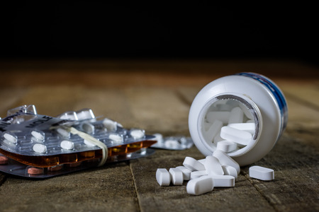 Medical tablets on a wooden table. White pills in plastic containers. Wooden table, black background.の写真素材