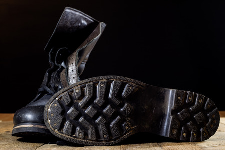 Old black Polish military boots on a wooden table. Black background.の写真素材