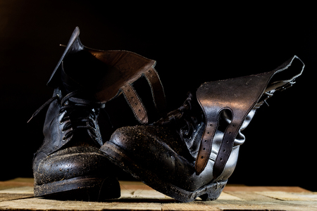 Muddy old military boots. Black color, dirty soles. Wooden table. Black backgroundの写真素材