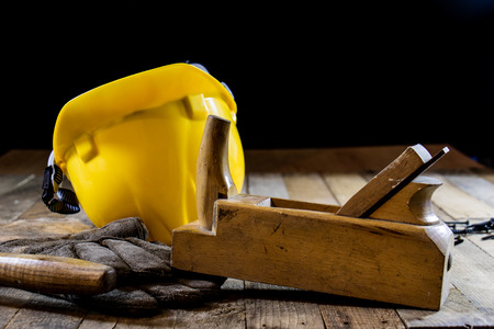 Yellow helmet and carpenter tools. Carpenter and old wooden table. Black backgroundの写真素材