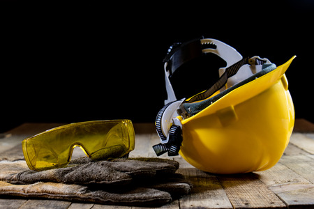 Yellow helmet and welding gloves. Black background and old wooden table.の写真素材