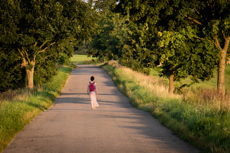Asphalt road leading among trees. In the middle of the road lonely person. Season of the summerの写真素材