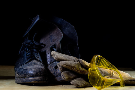 Workwear for a construction worker. Helmet, gloves, shoes and sunglasses on a wooden table. Black background.の写真素材