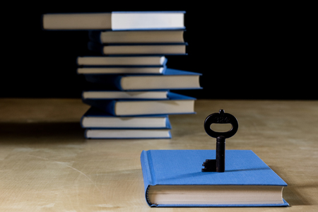 Heap of books reading on a wooden table. Beside lies and key. Black background.の写真素材