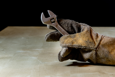 Hand in glove with tool for work in workshop. Hand protected by working coat. Workshop tool. Black background.の写真素材