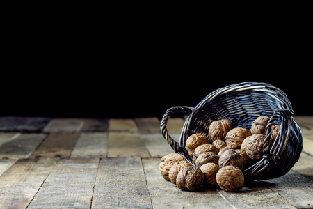 Tasty walnuts in a basket on a kitchen table. Autumn season. Wooden table, black backgroundの写真素材