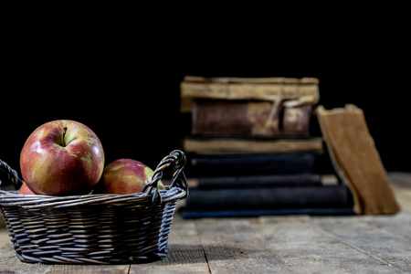 Tasty apples in basket on kitchen table. Old books lie next to apples in a garbage. Autumn season. Wooden table, black backgroundの写真素材