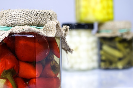 Tasty seasoned vegetables in jars. Kitchen pantry with mortar. White background, isolated.