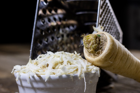 Root of parsley root on grater. Grate and parsley on the old kitchen table in the kitchen. Black backgroundの写真素材