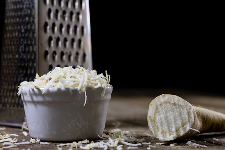 Root of parsley root on grater. Grate and parsley on the old kitchen table in the kitchen. Black backgroundの写真素材