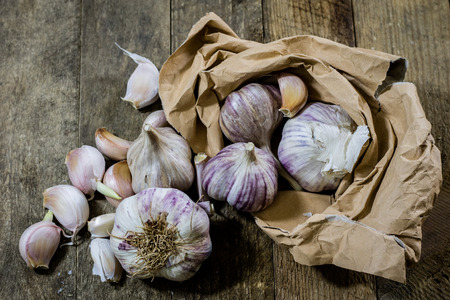 Garlic in a crumpled paper bag on a wooden table. Kitchen table with garlic in paper bag. black backgroundの写真素材