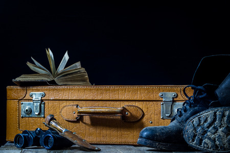 Old stylish suitcase. Military muddy shoes on a suitcase. Suitcase on a wooden table. Black backgroundの写真素材